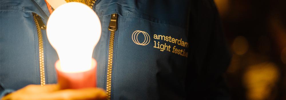 A volunteer with a light bulb in his hand, illuminating the white festival logo on his blue jacket.